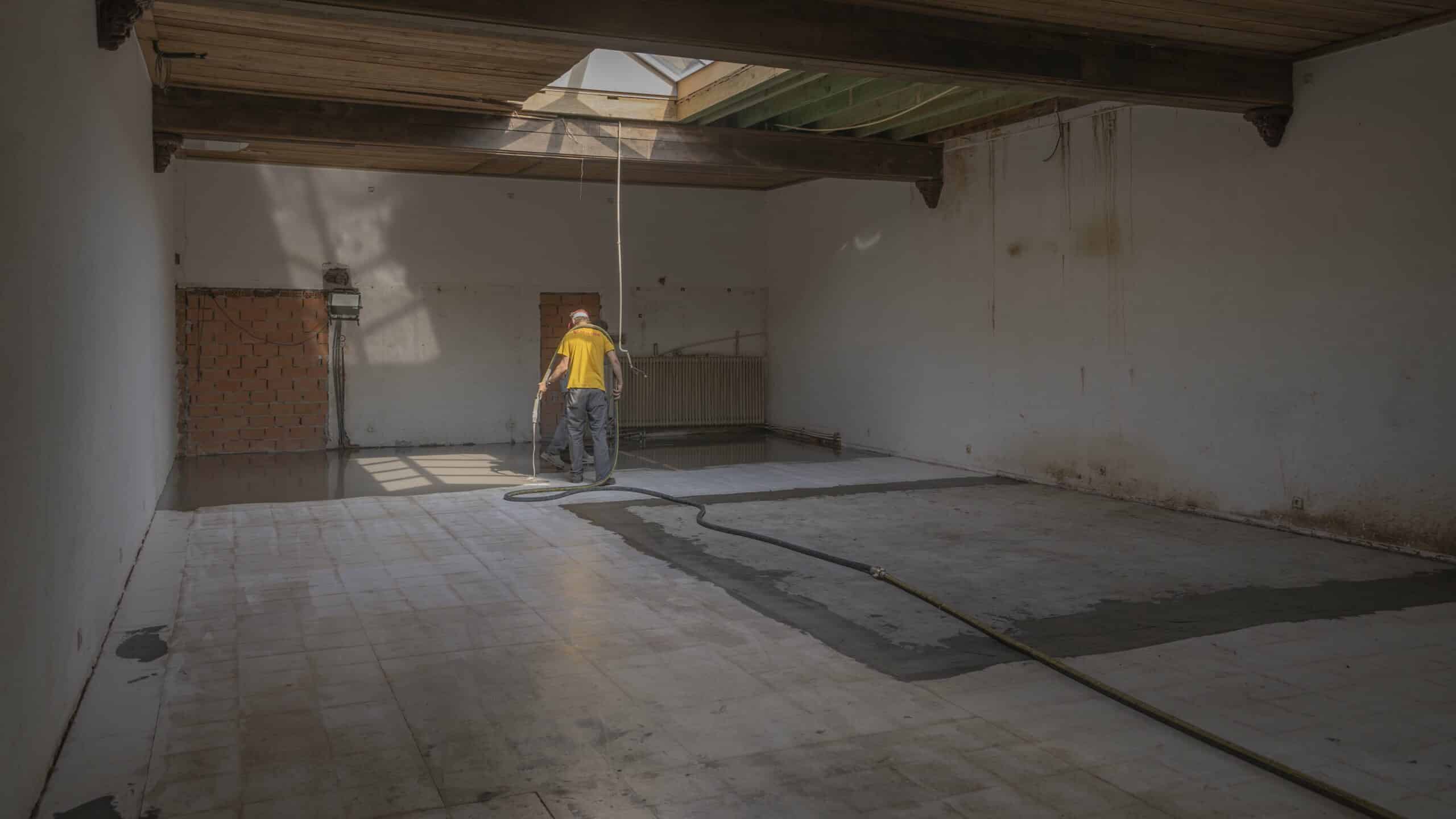 Man in Egalizer werkkleding brengt egalisatie laag aan in een gestripte ruimte.